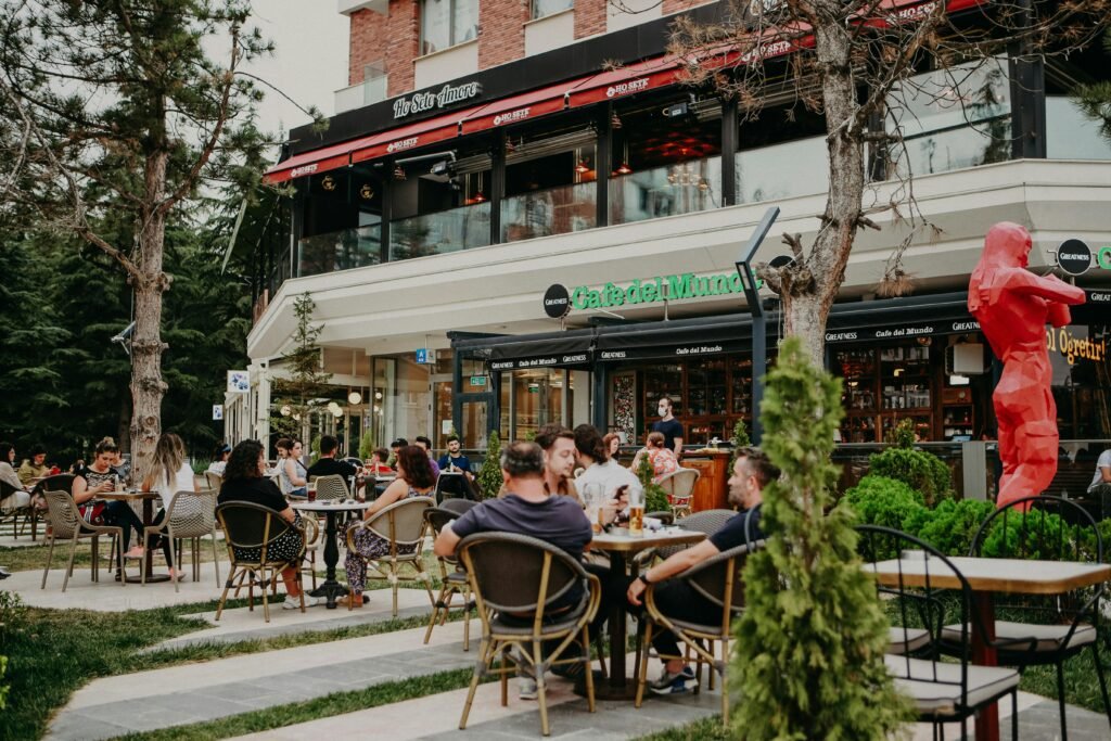 People enjoying a casual gathering at an outdoor cafe, surrounded by greenery and city atmosphere.